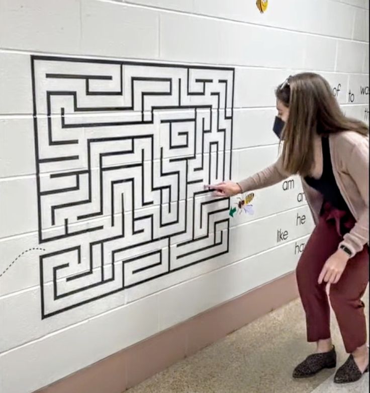 a woman wearing a face mask points at a wall with a maze drawn on it