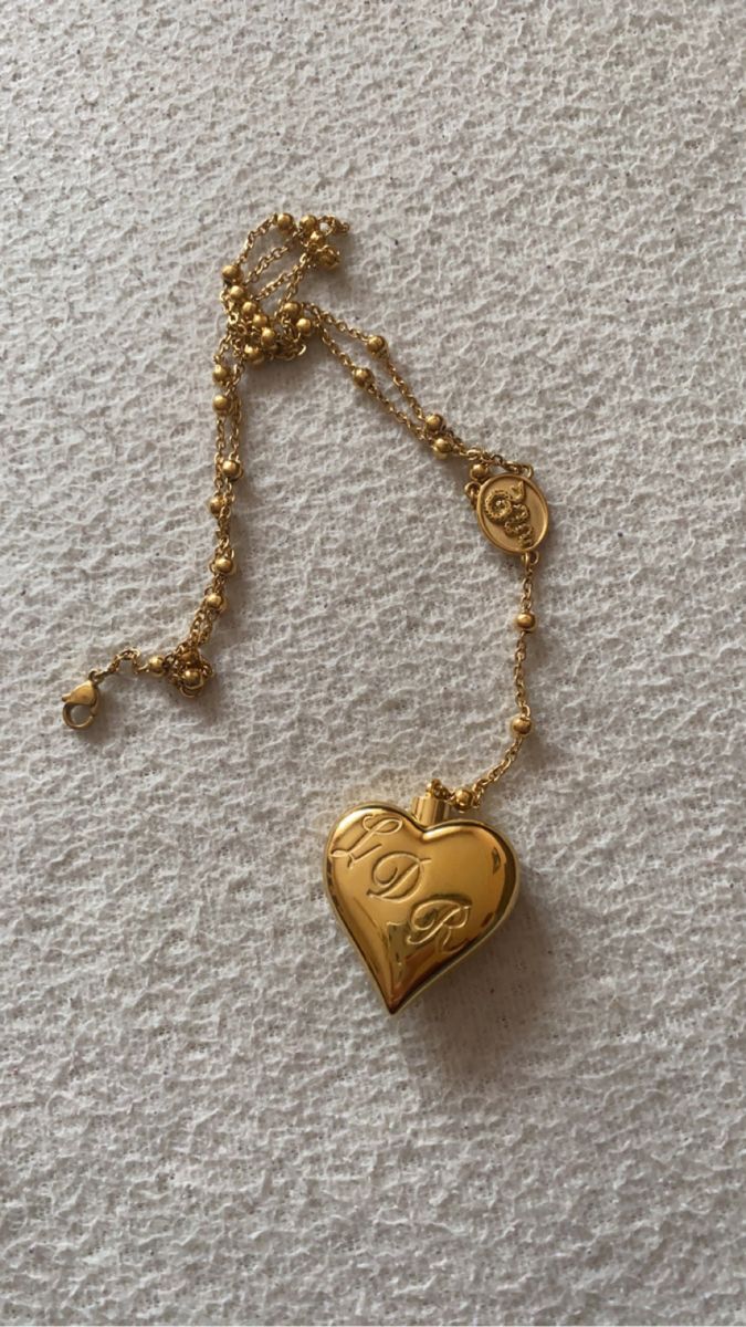 a gold necklace with a heart shaped locke hanging from it's side on a white surface