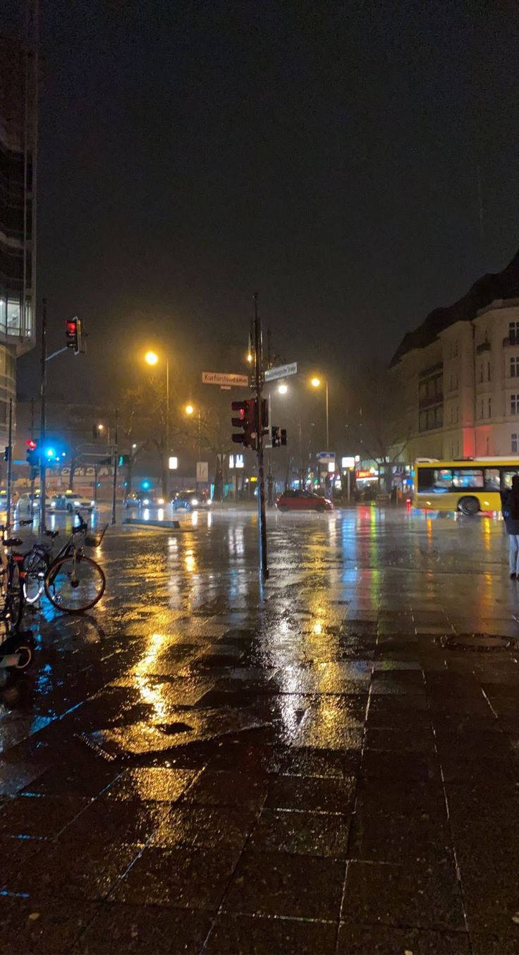 a city street at night with traffic lights and people walking on the sidewalk in the rain