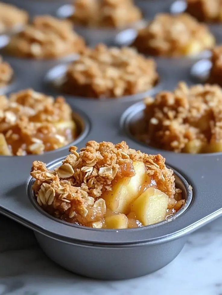 a muffin tin filled with apple crumbles and oatmeal topping