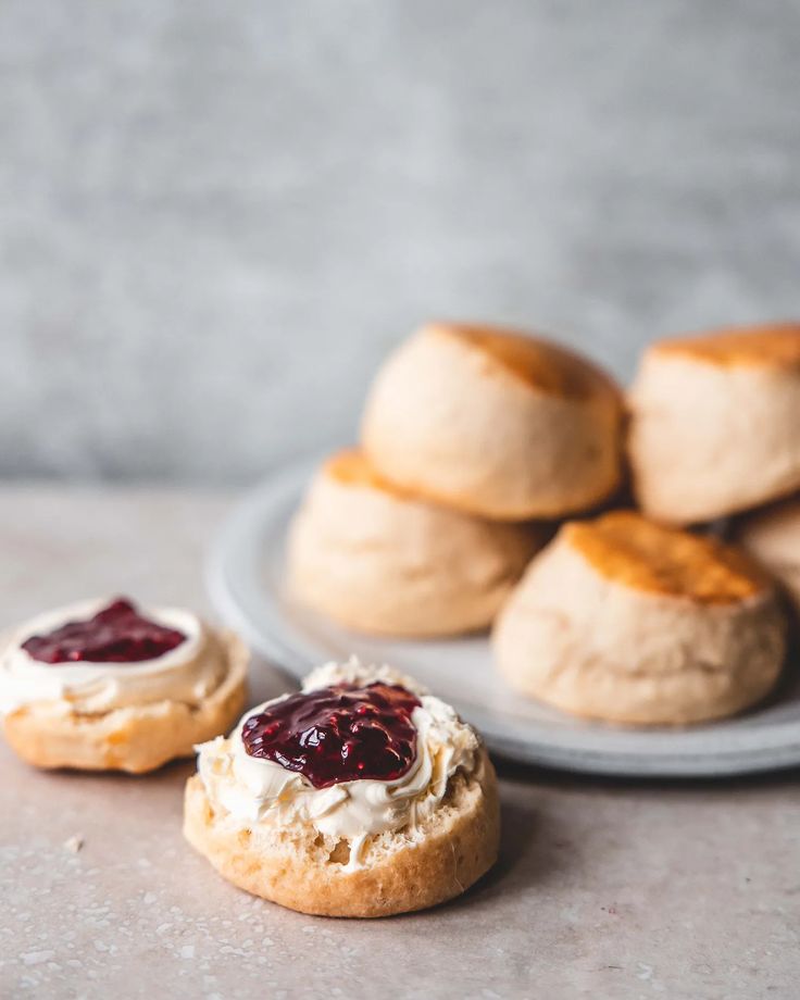 small pastries with jam on them sit on a plate next to some bread rolls