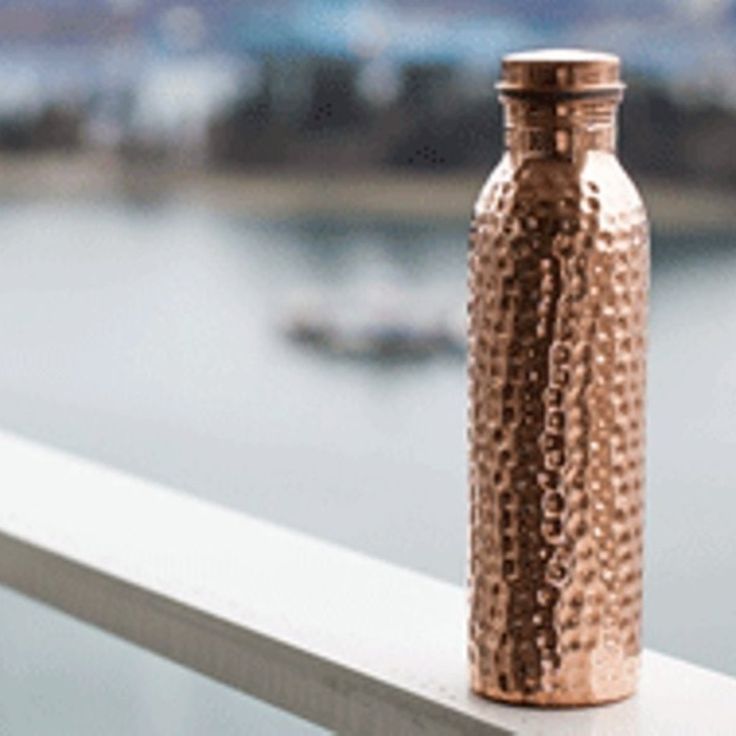 a copper colored metal bottle sitting on top of a white ledge next to a body of water