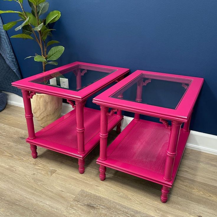 two pink end tables with glass tops on wooden floor next to blue wall and potted plant