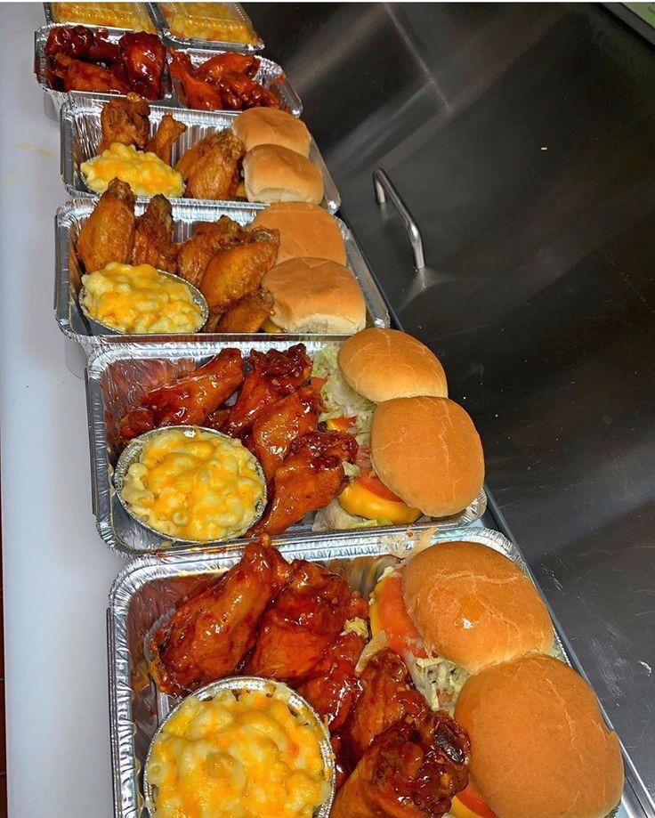 several trays of food are lined up on a counter top, including chicken sandwiches and macaroni and cheese