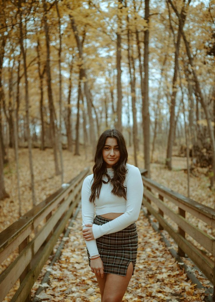 a woman is standing on a bridge in the woods with her arms crossed and looking at the camera