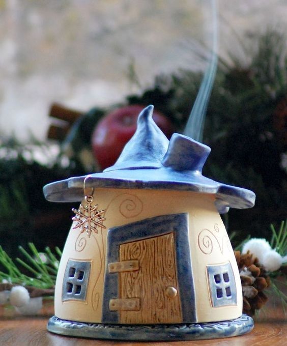 a small toy house with a blue roof on top of a wooden table next to pine cones