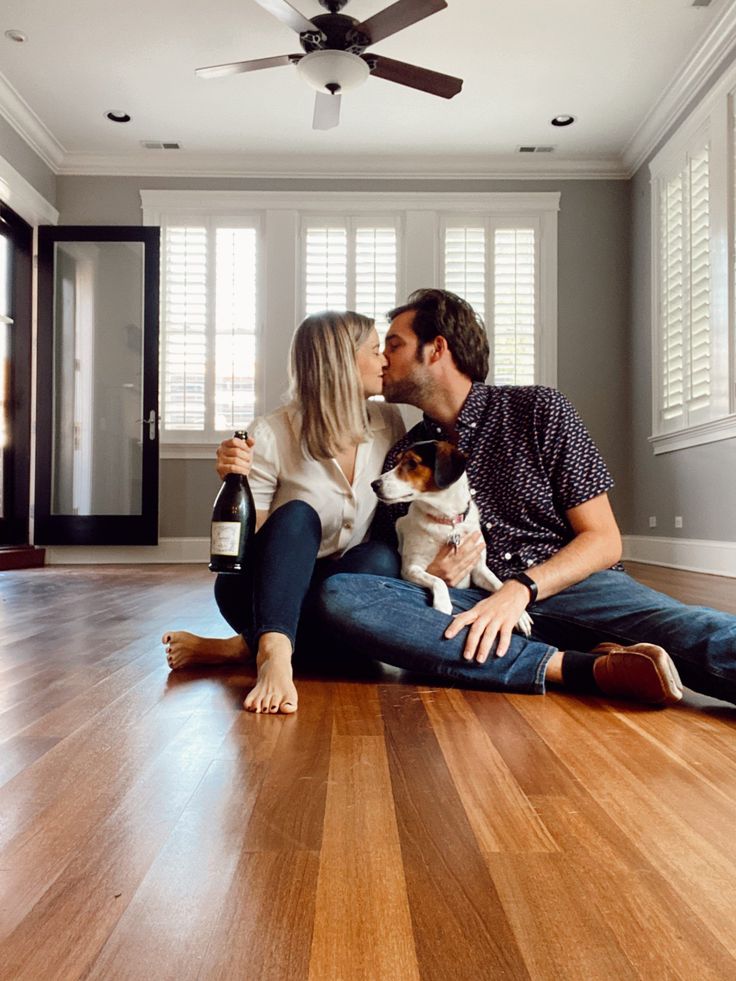 a man and woman sitting on the floor kissing with a dog in front of them