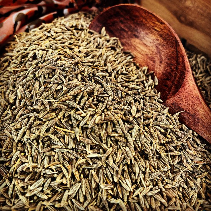 a wooden spoon filled with cumsins on top of a pile of dried seeds