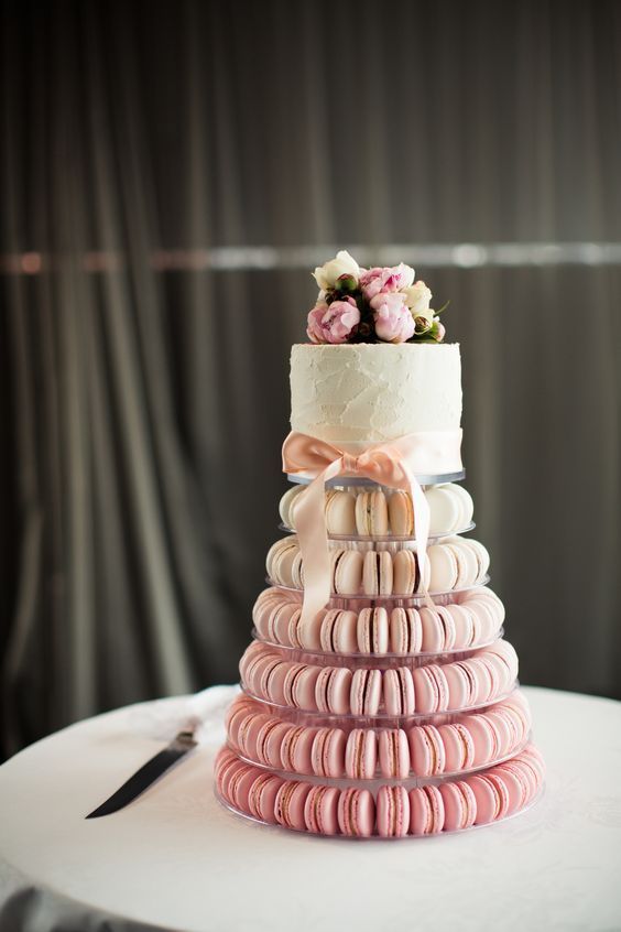 a wedding cake with pink macaroons and flowers on top is stacked in the shape of a stack