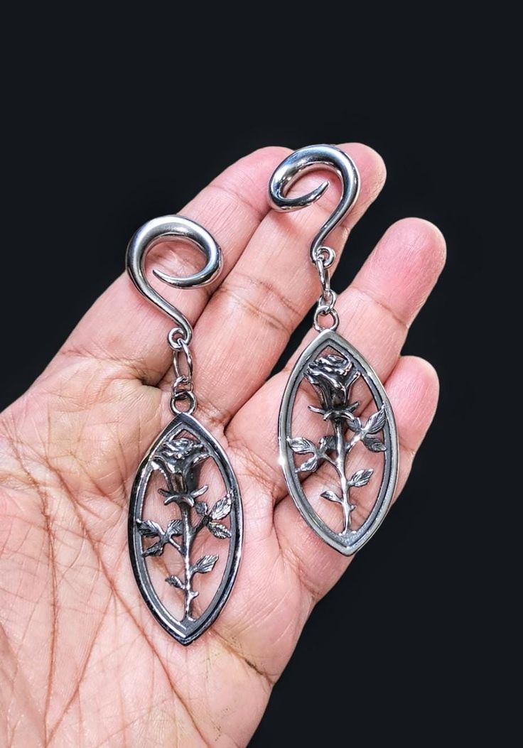 a pair of silver earrings sitting on top of a persons hand in front of a black background