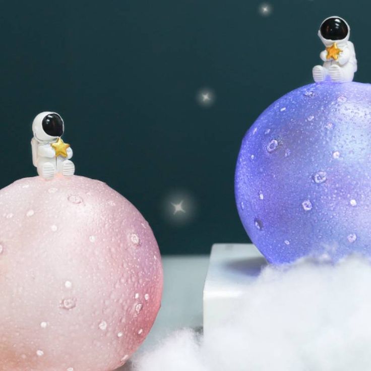 two snowmen are sitting on top of balls in the air, one is pink and one is blue