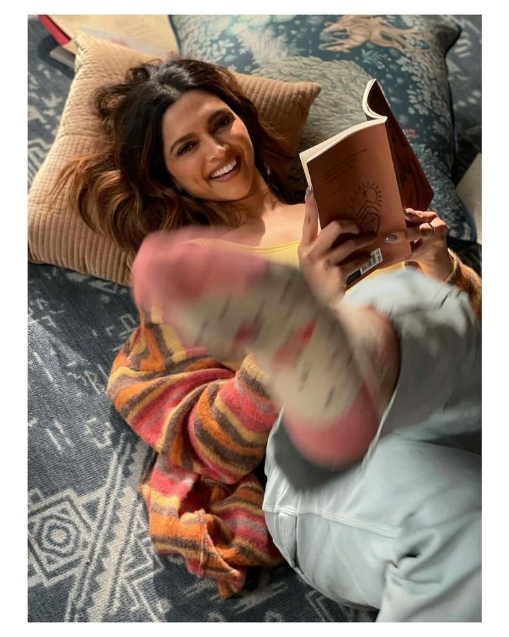 a woman laying on top of a couch holding an open book in her right hand