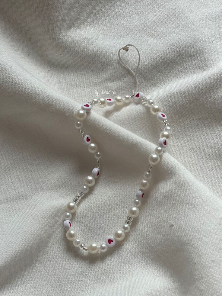 a white beaded necklace with red and white beads is laying on a white sheet