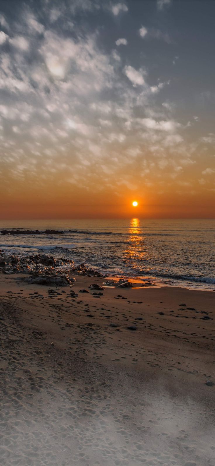 the sun is setting over the ocean with clouds in the sky and sand on the beach