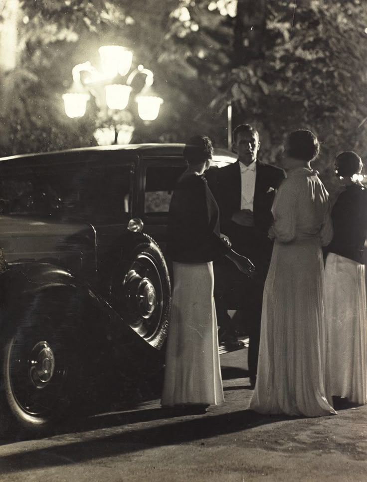 an old black and white photo of people standing in front of a car at night