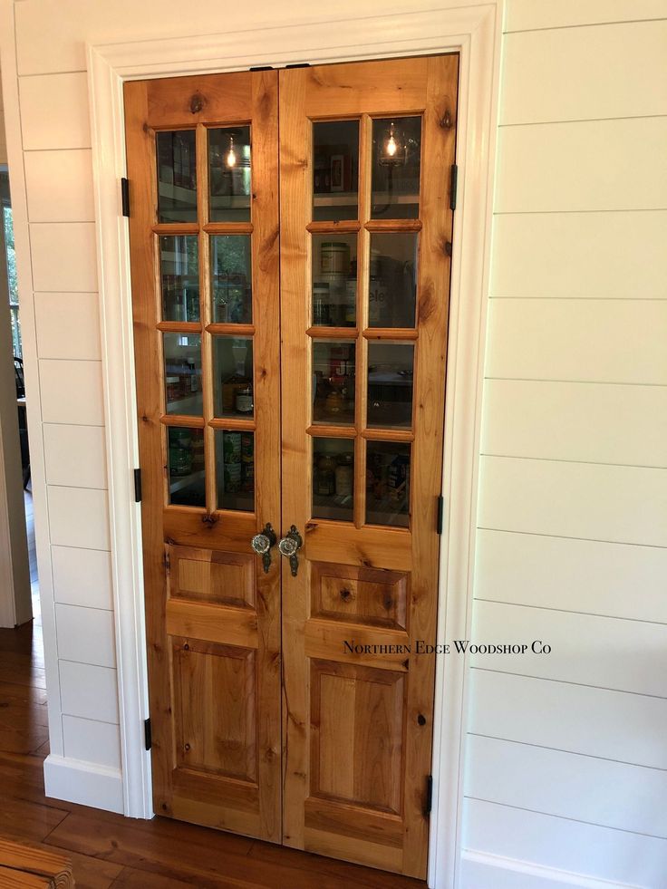 two wooden doors with glass panels in a white wall and wood flooring on the other side