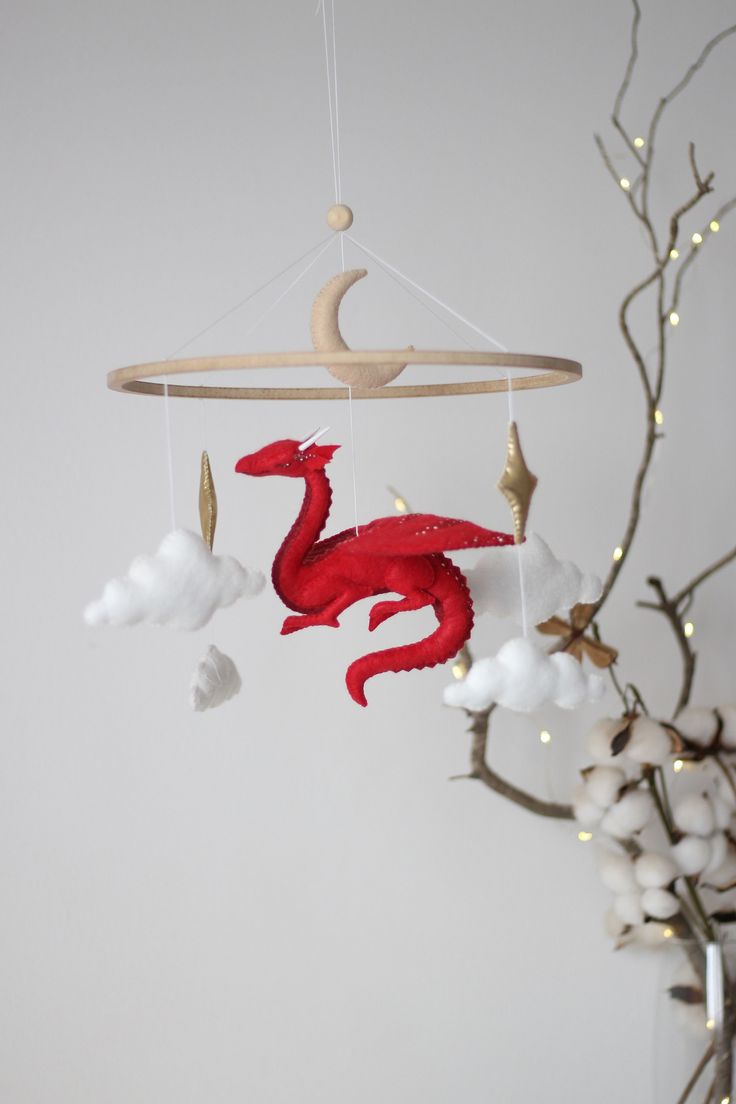 a red dragon mobile hanging from a branch with white flowers in front of the wall