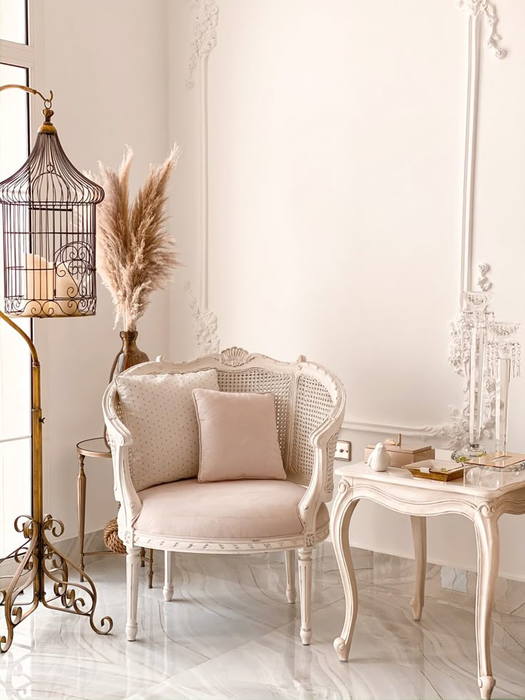 two chairs and a table with a birdcage on it in a white room