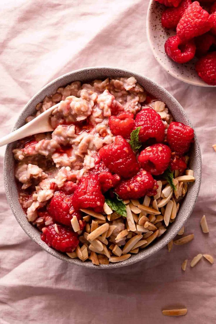 a bowl of oatmeal with raspberries and almonds on the side