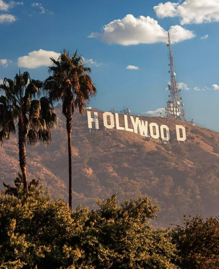 the hollywood sign is surrounded by palm trees and mountain in the background, with a radio tower on top