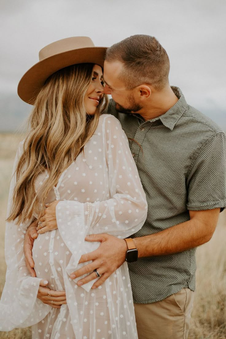 a pregnant couple cuddles in the middle of a field