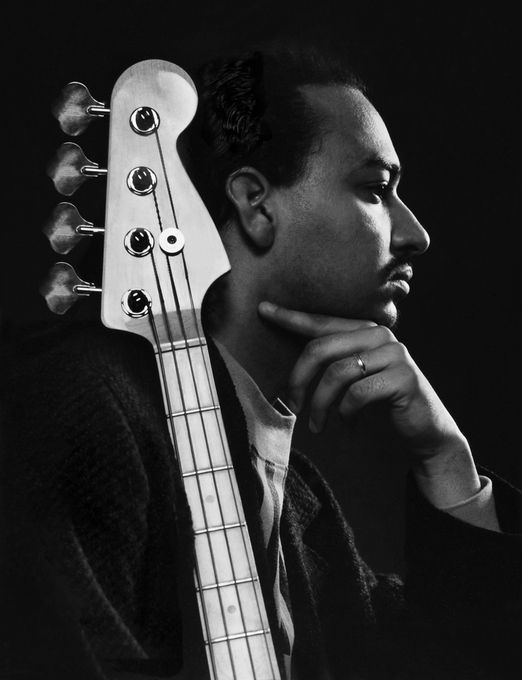 a black and white photo of a man with a bass guitar on his head, looking to the side