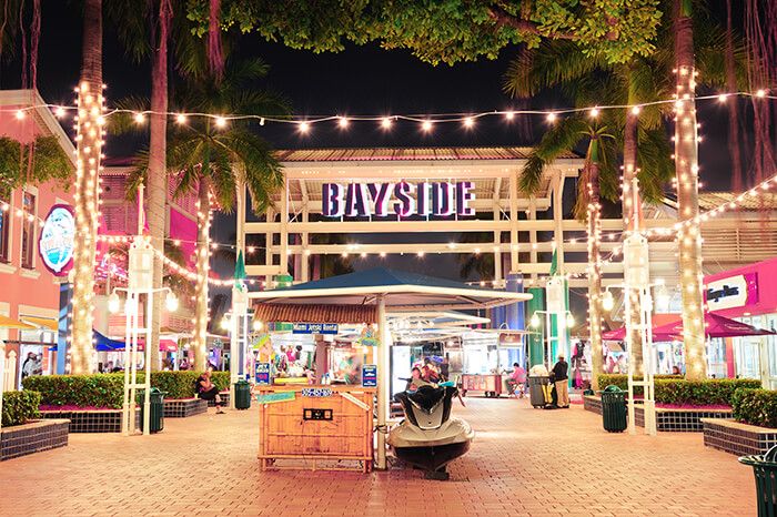 the entrance to bayside shopping center at night with lights strung from trees and palm trees