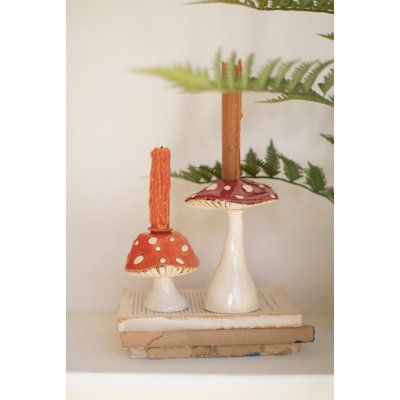 two small mushrooms sitting on top of a book next to a fern plant and candle holder