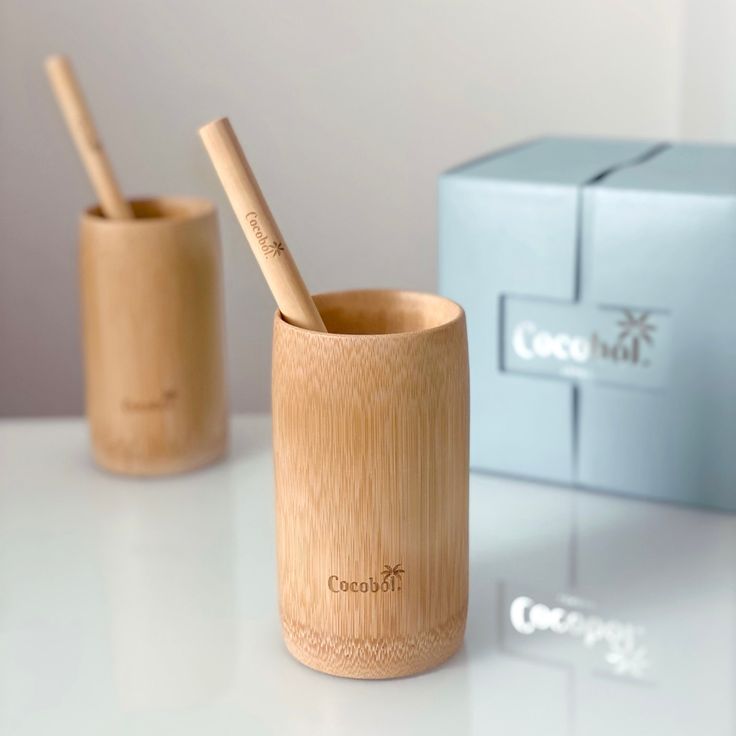 two bamboo toothbrushes in a wooden cup next to a blue box with the word coconut beach written on it