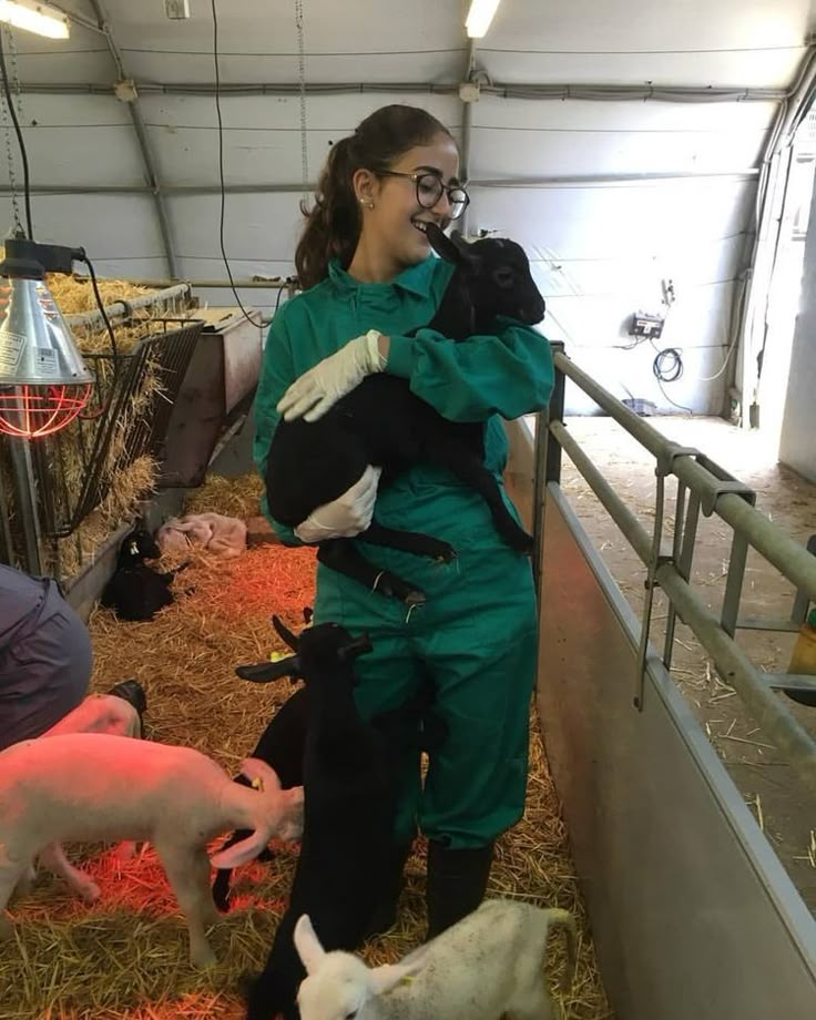 a woman in green jumpsuits standing next to some animals and feeding them on hay