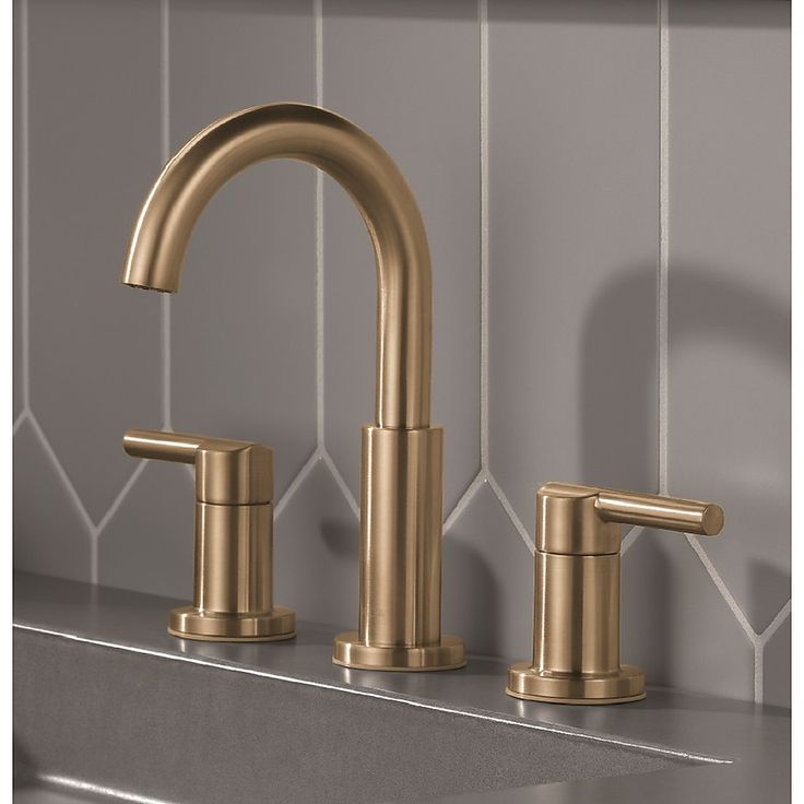 a gold faucet with two handles on a gray tiled wall