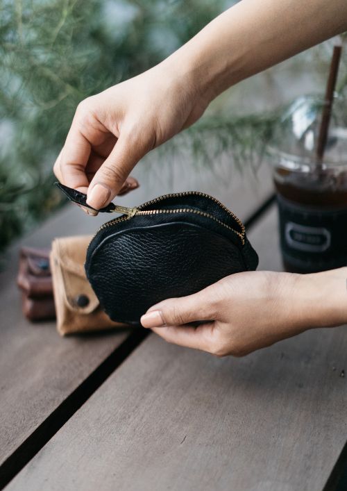 a person holding a black purse on top of a wooden table next to a cup