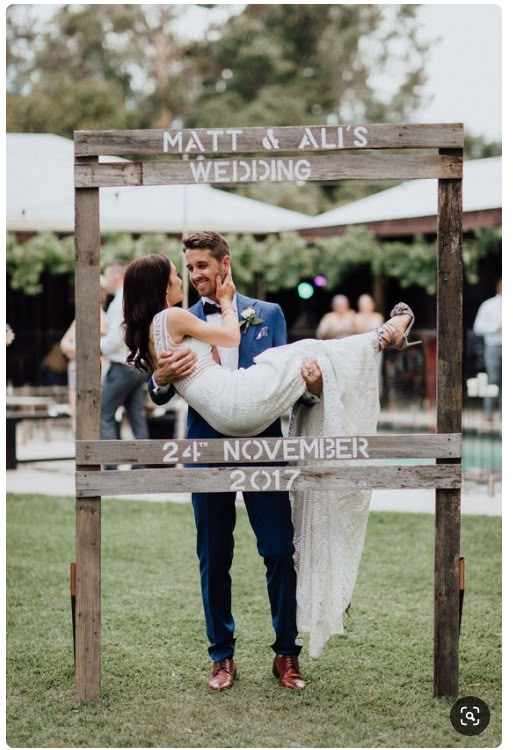 a newly married couple standing in front of a wooden sign