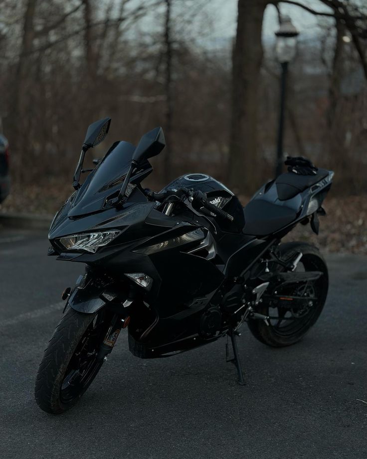 a black motorcycle parked on the street in front of some trees with no one around it