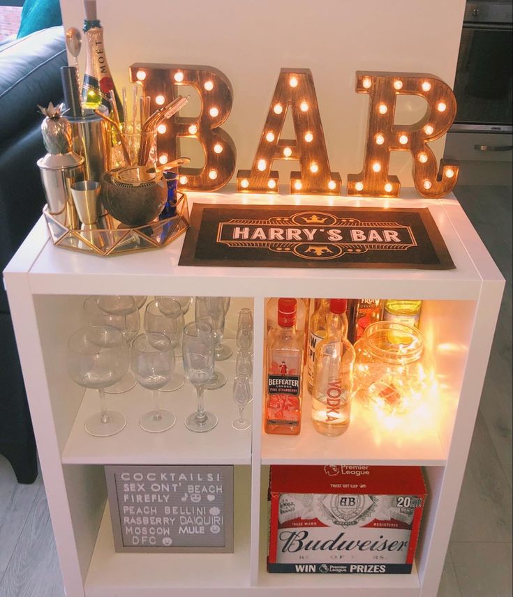 an illuminated bar sign on top of a white shelf filled with liquor bottles and glasses