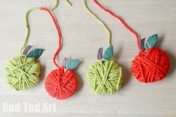 three crocheted apples hanging from strings on a table