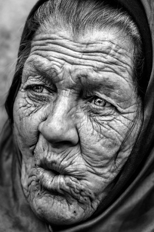 an old woman with wrinkles on her face and headdress, looking at the camera