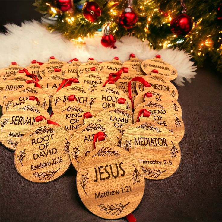 twelve wooden christmas ornament with names and date printed on them, sitting in front of a christmas tree