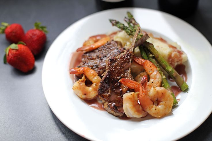 a white plate topped with meat, shrimp and asparagus next to strawberries