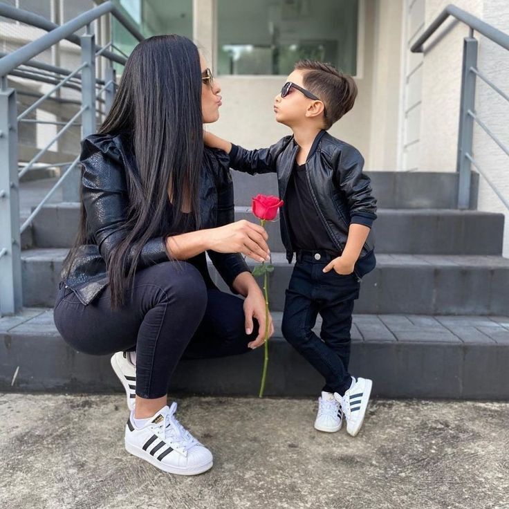 a woman kneeling down next to a little boy who is holding a red rose in his hand