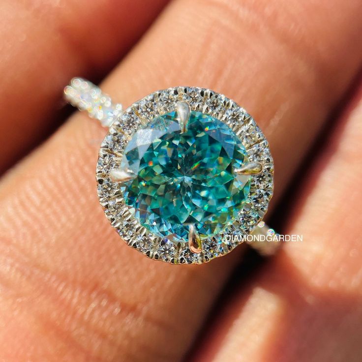 a woman's hand holding a ring with an aqua blue and white diamond in it