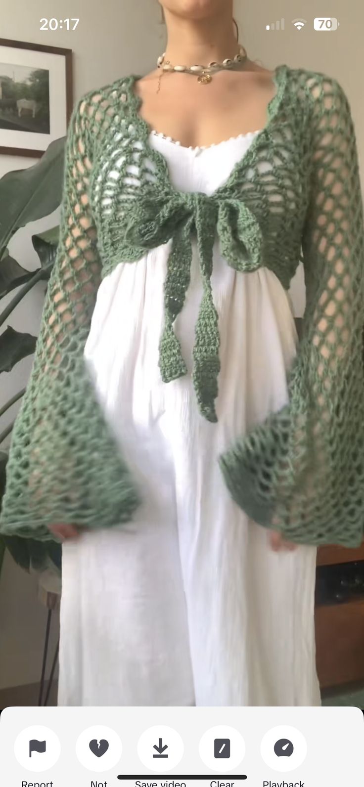 a woman wearing a white dress and green crochet shawl with her hands in her pockets