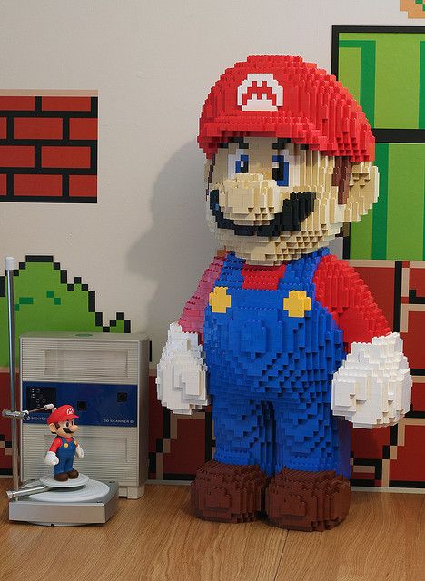 a large lego mario is standing next to a nintendo wii game controller on a table