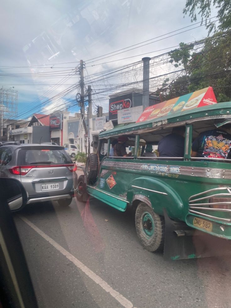 an old green bus is driving down the street with other cars and trucks behind it