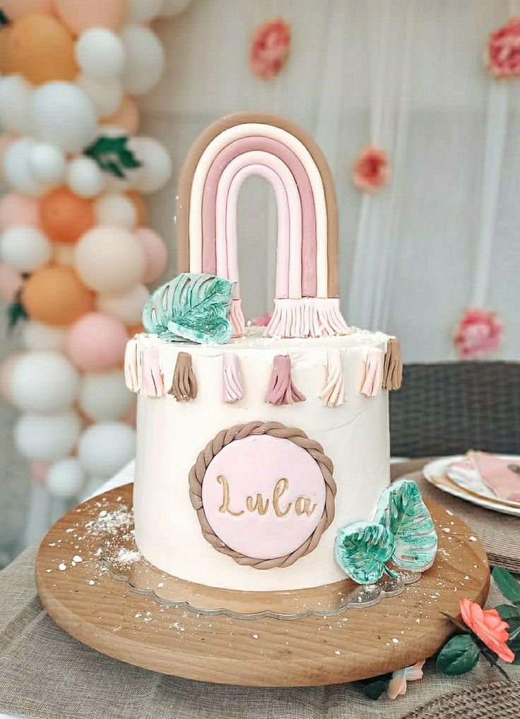 a pink and white cake sitting on top of a wooden platter next to balloons