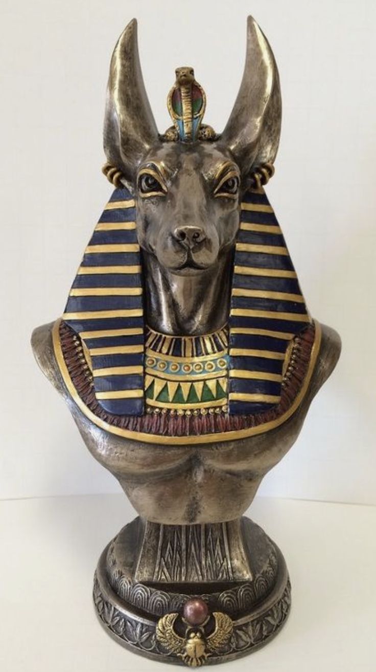 an egyptian statue is sitting on a white surface and has gold colored decorations around its neck