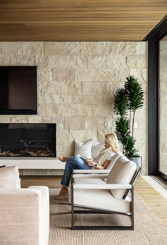 a woman sitting on a chair in front of a fireplace with a tv above it