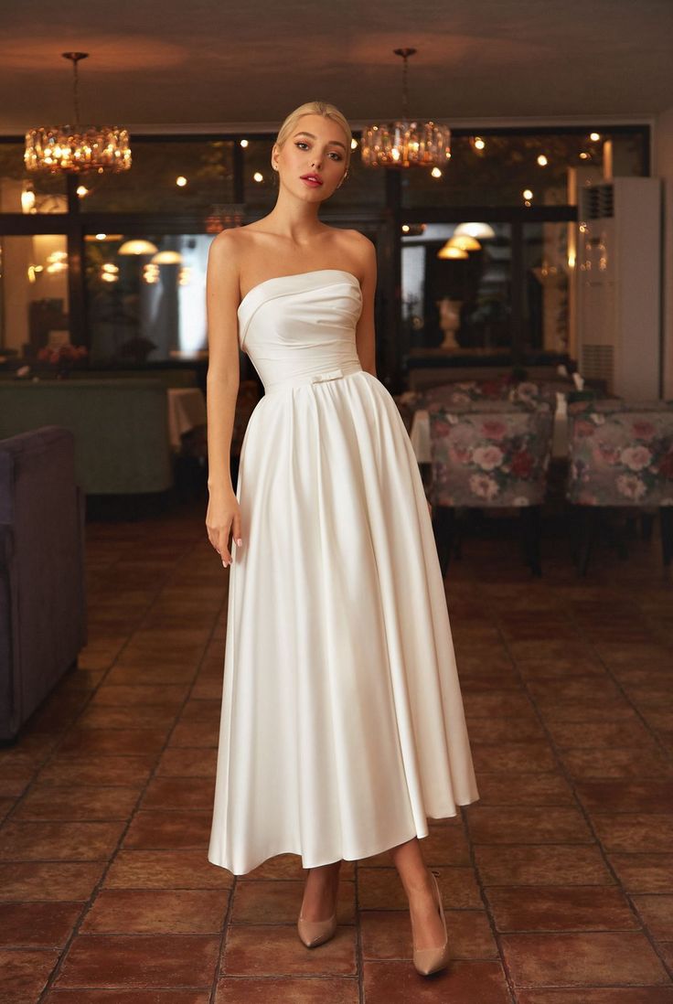 a woman wearing a white dress standing in a room with chandeliers on the ceiling