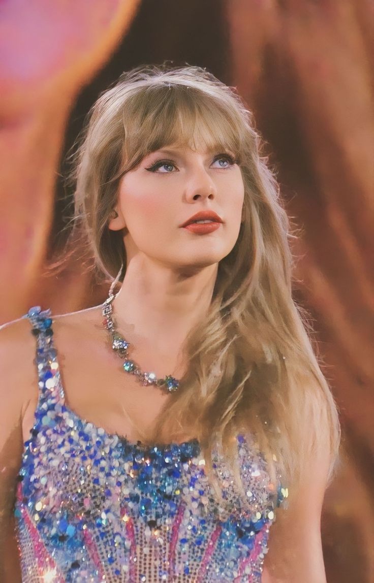 taylor swift wearing a blue and pink beaded dress in front of a stage backdrop