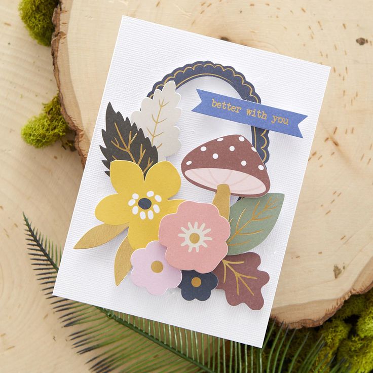 a close up of a greeting card with flowers and leaves on it next to a tree stump